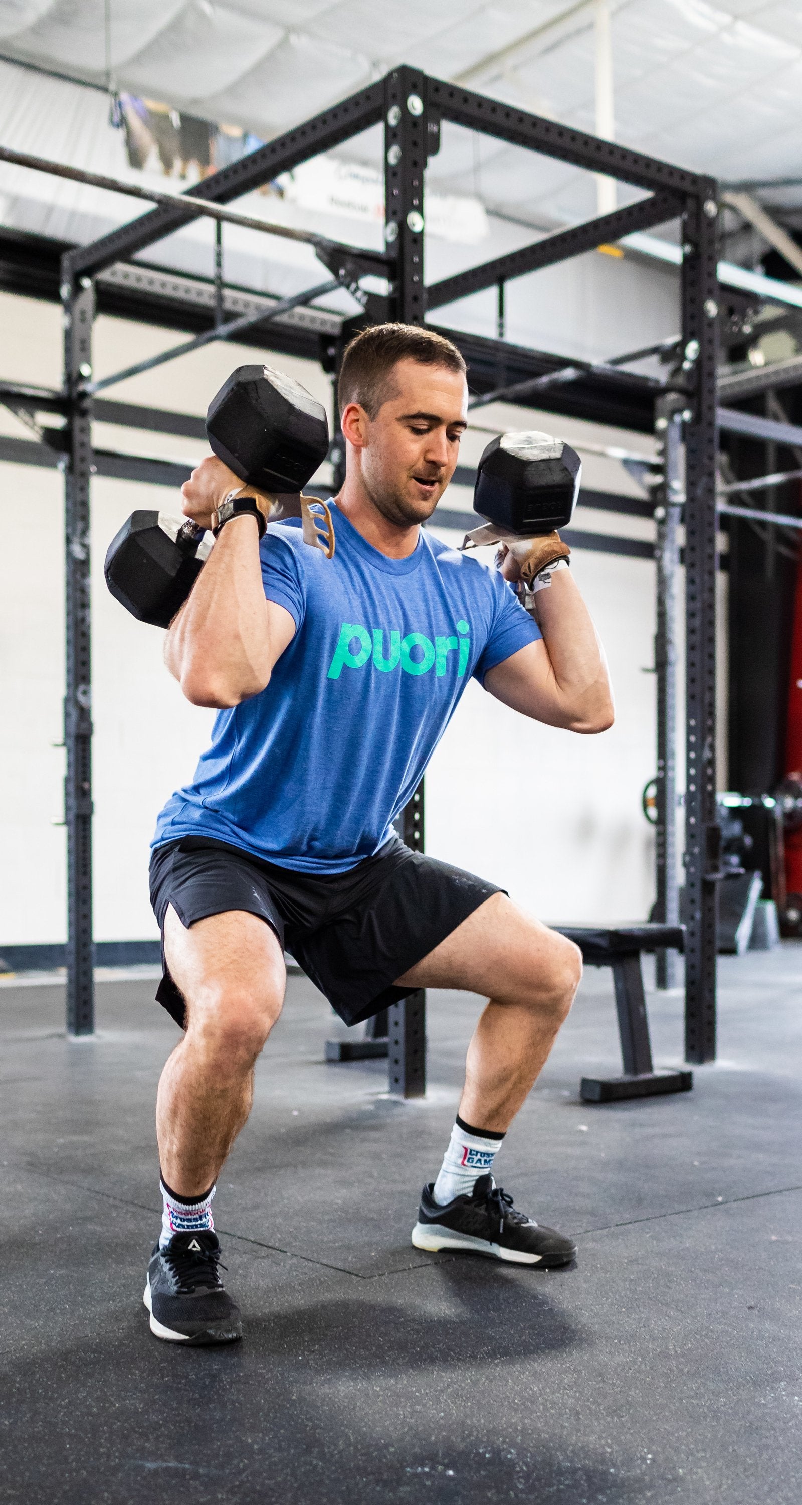 Man in a Puori t-shirt doing a dumbbell front squat inside a gym power rack.